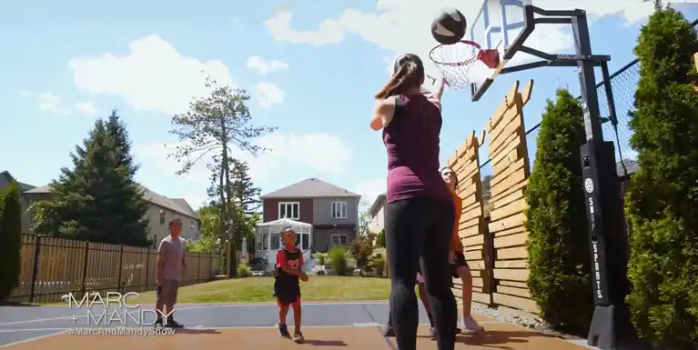 A family enjoying a game of basketball on a custom backyard court under clear blue skies