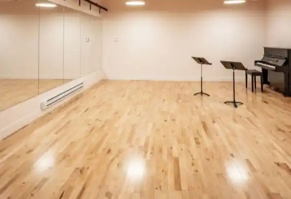 A bright dance rehearsal studio with a professional Junckers hardwood floor, wall-length mirrors, and a piano.
