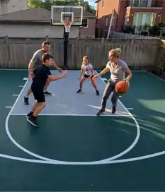 A family of four happily playing basketball on a green and gray backyard sports court.