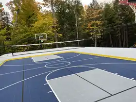 A premium 2,160 sq ft custom backyard court in Parry Sound, featuring unique blue and gray zones for basketball, hockey, pickleball and volleyball. Perimeter dasher boards and high containment netting.